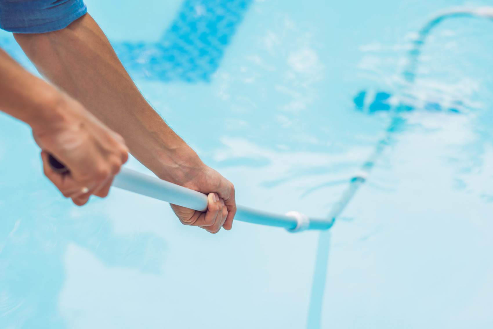 Cleaner of the swimming pool . Man in a blue shirt with cleaning equipment for swimming pools, sunny.